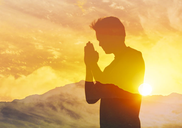 Homen agradecendo com as maos juntas e ao fundo um por do sol